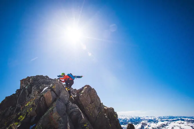 Man with skis on back climbing to summit of mountain