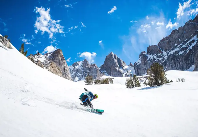 Man snowboarding down from mountain ridge in California backcountry