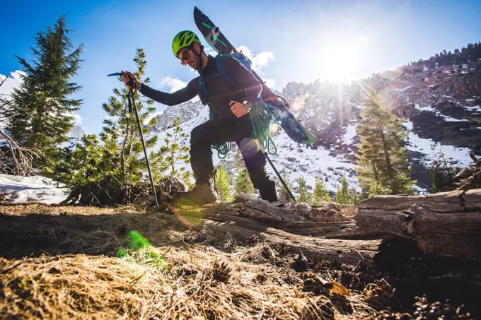 Low angle of man walking in mountains with skis on backpack