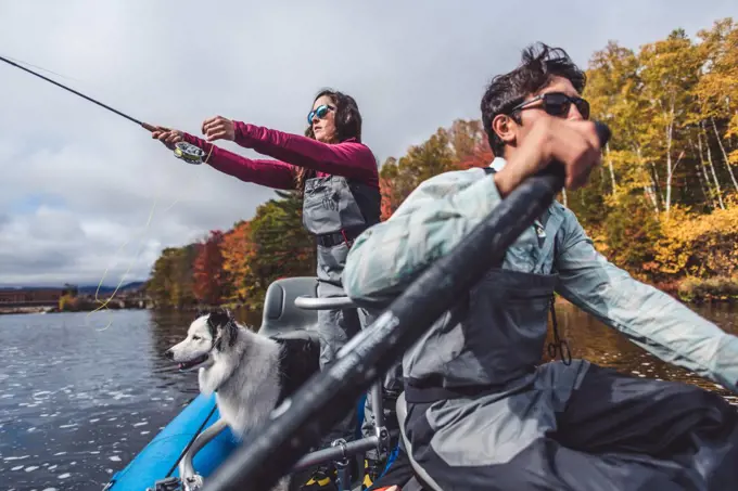 Man and woman anglers with dog in a boat during foliage season