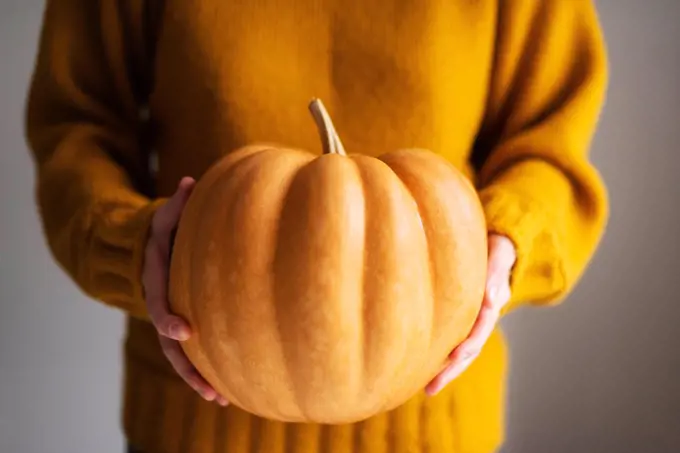 woman holding fresh pumpkin while standing in white background