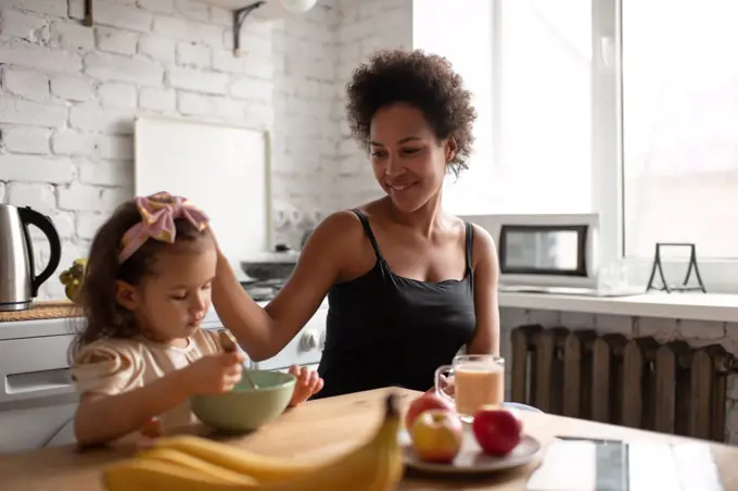 Ethnic mother stroking daughter during breakfast