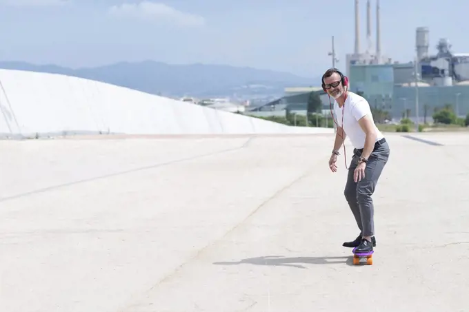 Bearded man with headphones enjoys riding a skateboard through city