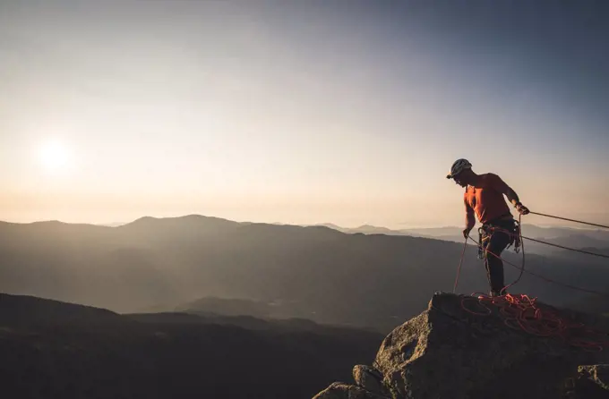 Man belaying with climbng ropes at sunrise in mountains