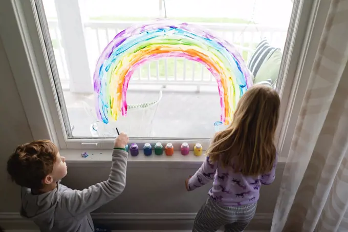 top down view of siblings painting rainbow on living room window