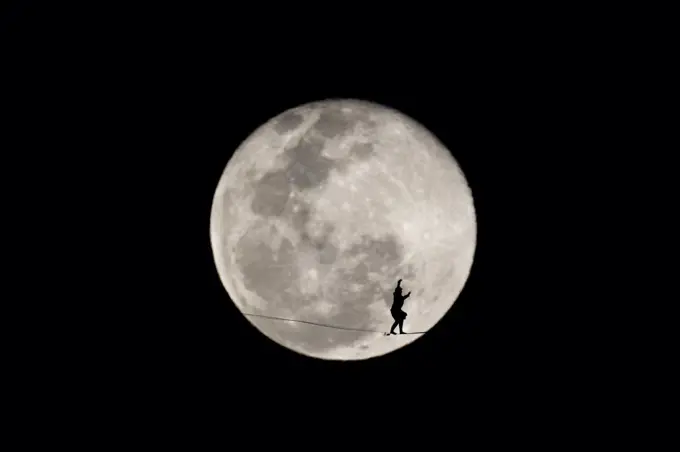 One person walking on a highline in front of the winter full moon