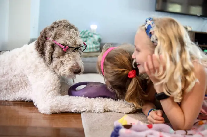 two girls playing with large brown and white dog on floor at home