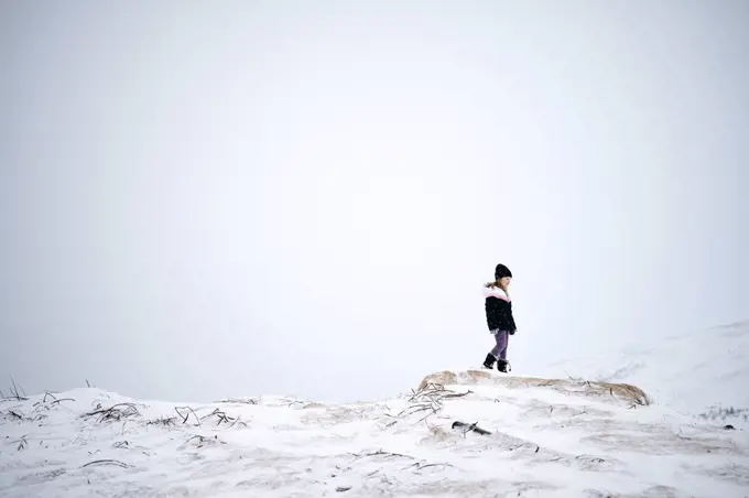 Unrecognizable kid in warm clothes walking on snowy mountain slope