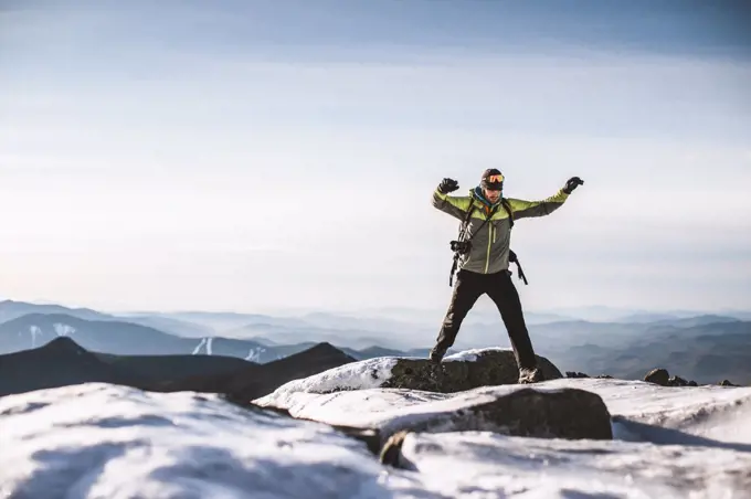 Man with camera jumps from icy rock on mountain summit in winter