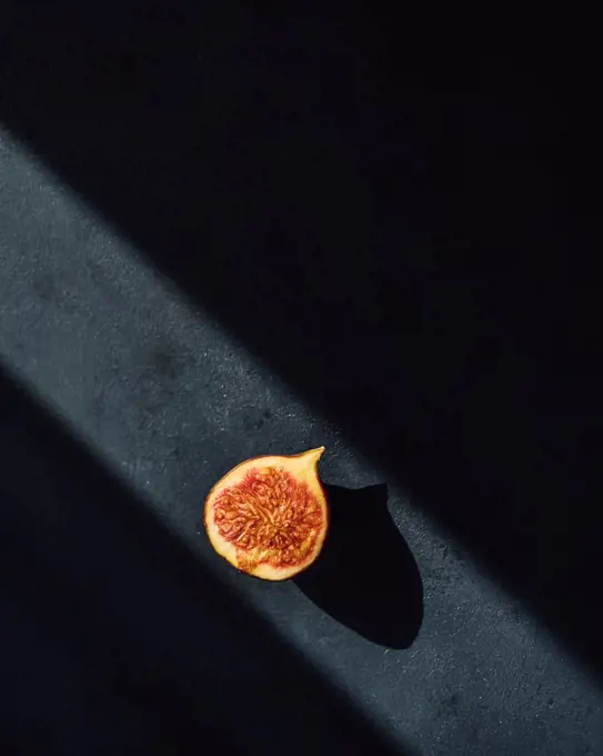 Minimal photo of a fig half on dark background in a ray of light