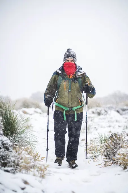 A man with face covered treks under heavy snow