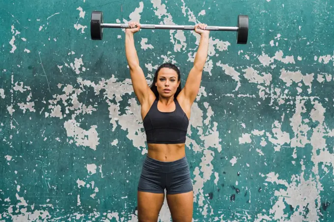 female athlete performing shoulder press at wall of outdoor gym