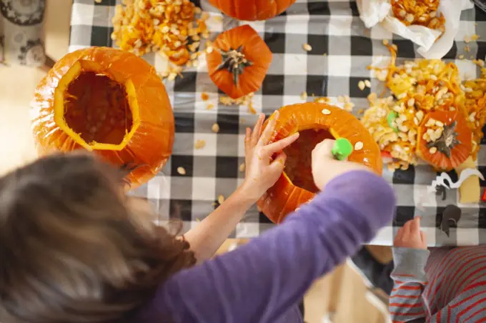 Above head view of kids scooping out pumpkin seeds at table