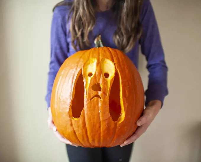 Close up of tween girl holding up carved pumpkin of dog against wall