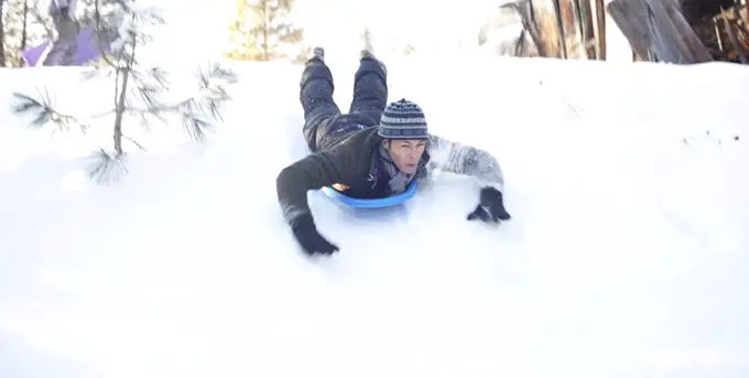 Man sliding down snowy hill in sled