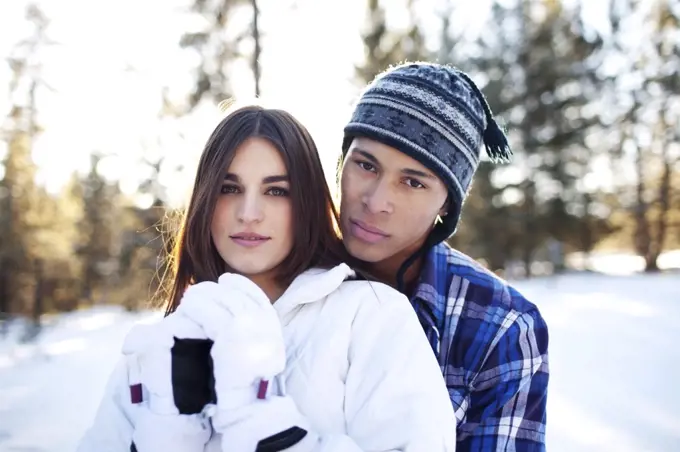 Couple embracing while looking at camera in snowy forest