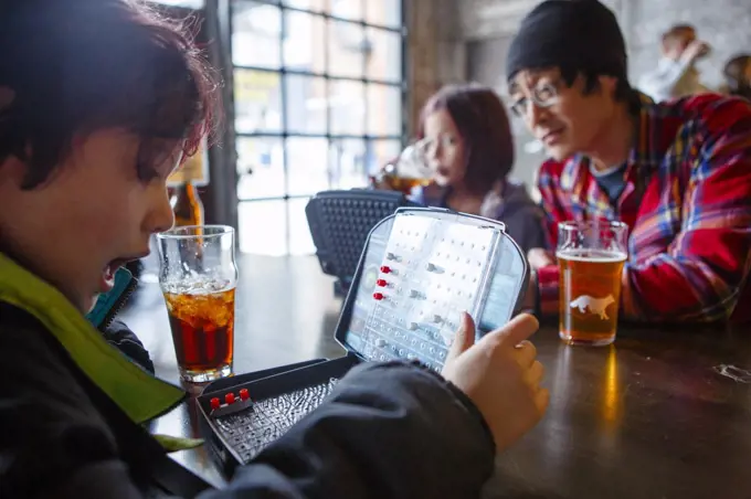 A little boy sits in a restaurant with sister and dad playing game