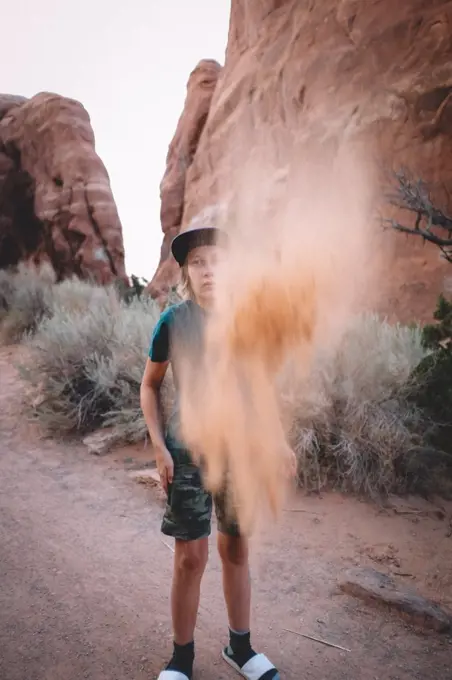 Boy Tosses Sand into the Air Surrounded by Sandstone and Desert