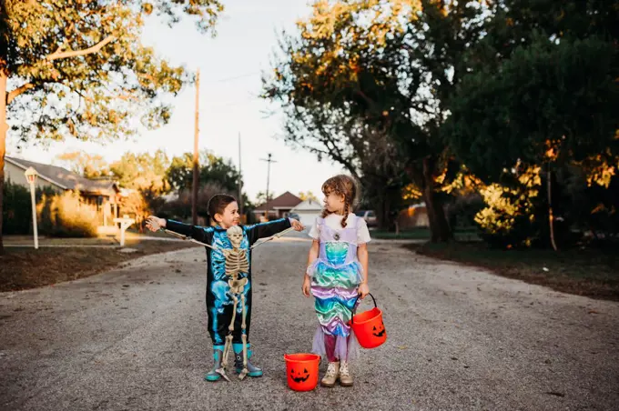 Young kids standing in street dressed up for halloween at sunset