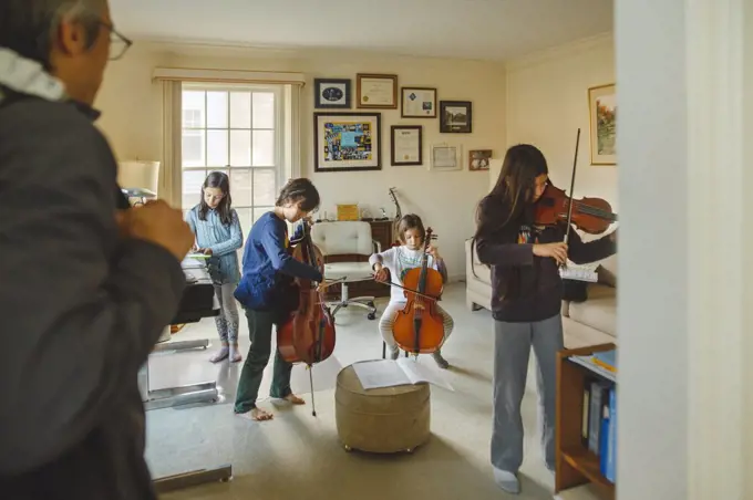 A group of children with stringed instruments play as father watches