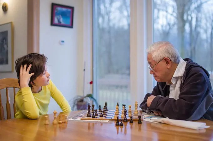 A grandfather carefully studies a chessboard while grandson looks on