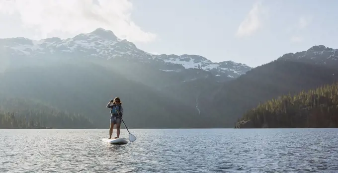 Female adventurer paddle boarding on lake against snowy mountain ridge