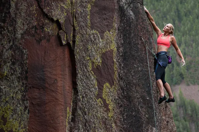 Female rock climber with wind blown hair rests while leading route