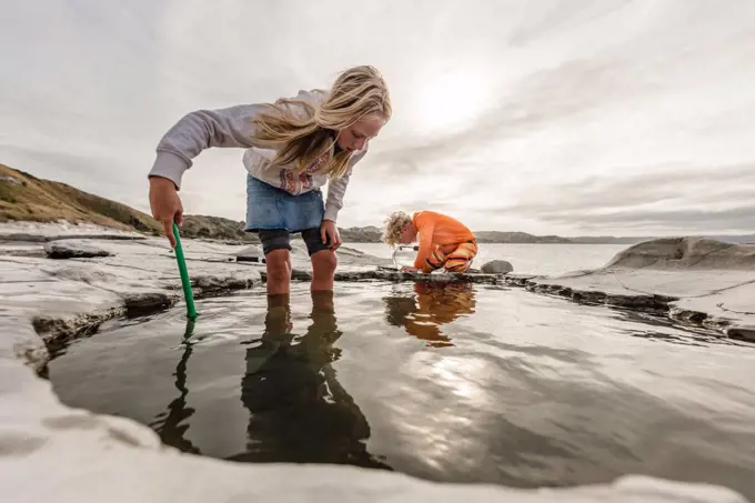 Two children exploring rock pools together in New Zealand