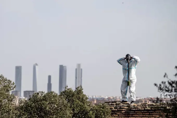 A man in a EPI virus suit and a gas mask on his face with the city in the background