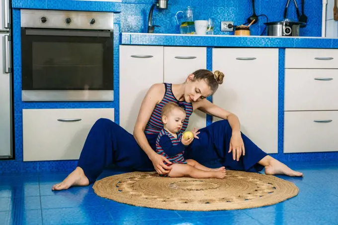 Young mom and her baby girl playing with apple in the kitchen