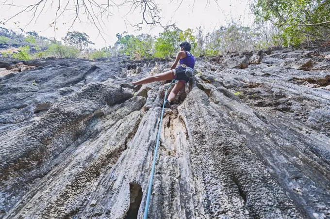 woman climbing steep limestone cliff in Laos