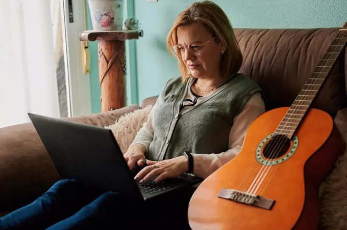 Middle-aged woman learn to play the guitar with a laptop at home