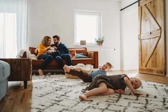 Siblings having fun in living room parents sit on sofa with baby