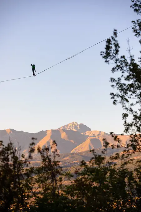 Slackliner walking over Gran Sasso with trees in the foreground