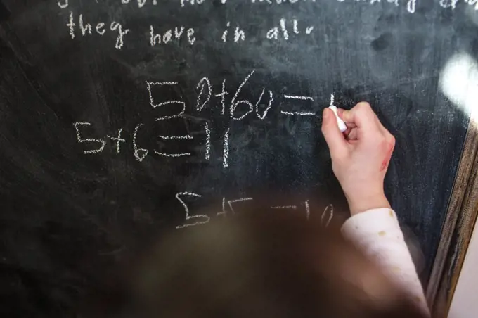 close-up of a small child writing mathematical equations on chalkboard