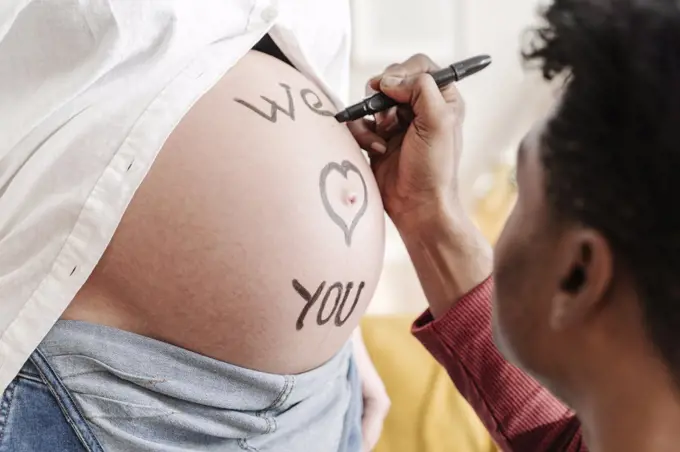 Husband drawing the phrase we love you on the belly of his pregnant wife. Parenthood concept