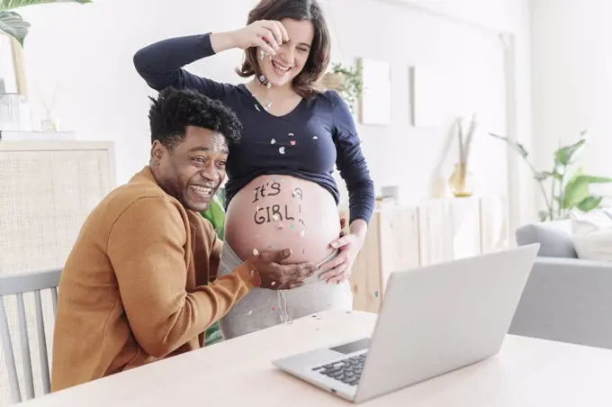 Husband and pregnant wife celebrating in front of a laptop. Parenthood concept