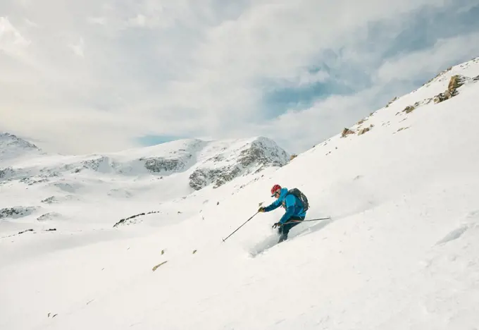 Male skier skis down a powdery slope on a sunny day in the backcountry