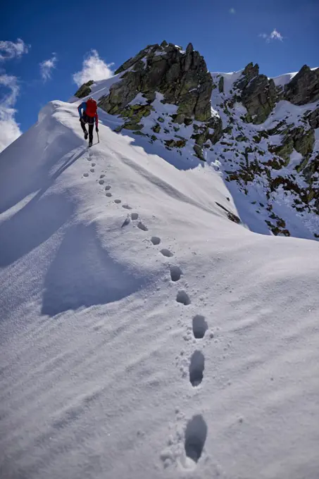 Man climbing a snowy mountain on a sunny day in Devero, Italy.