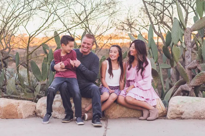 Family of four sitting on a rock and smiling at each other.