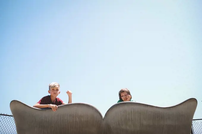 Boys Peek Over a Cement Whale Tale Bench on a Summer Day