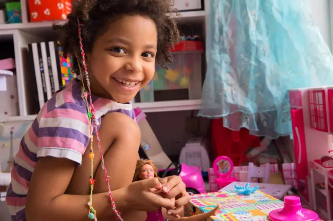 Mixed race little girl playing with doll smiling in a playroom