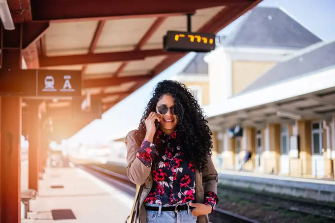 Happy young African girl talking on cell phone at train station in Europe