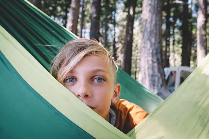 Blonde Tween with Big Blue Eyes Peeks from behind a Green Hammock