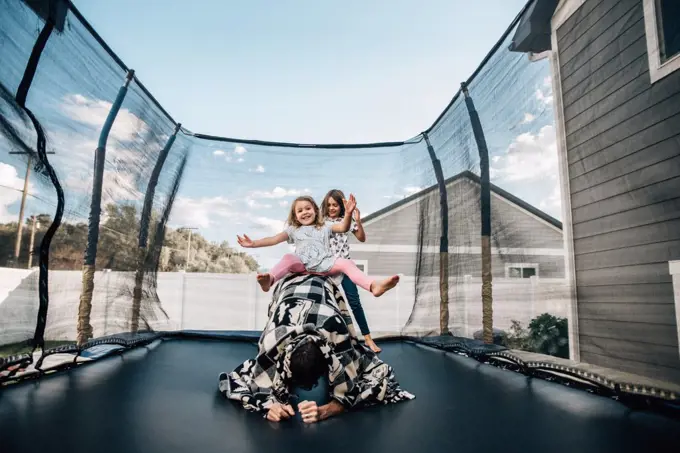 Daughters playing with their dad on the trampoline in the summer