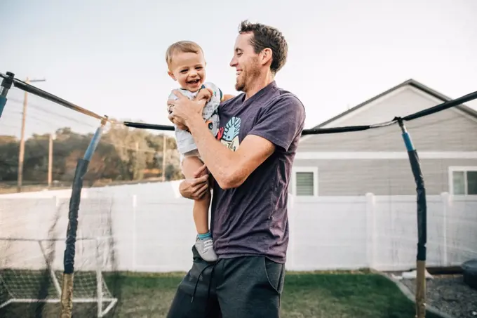 Dad laughing on trampoline with toddler son