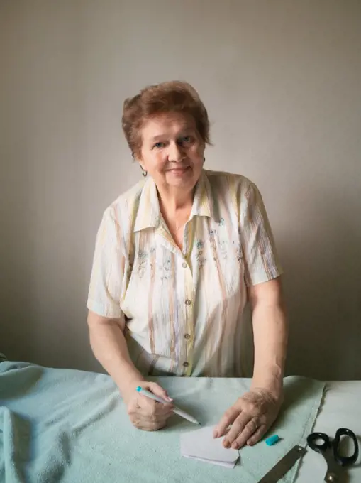 An elderly woman makes a pattern of a medical mask on a fabric