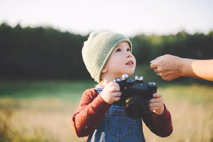 Little boy  holding film camera  in a large field in the country