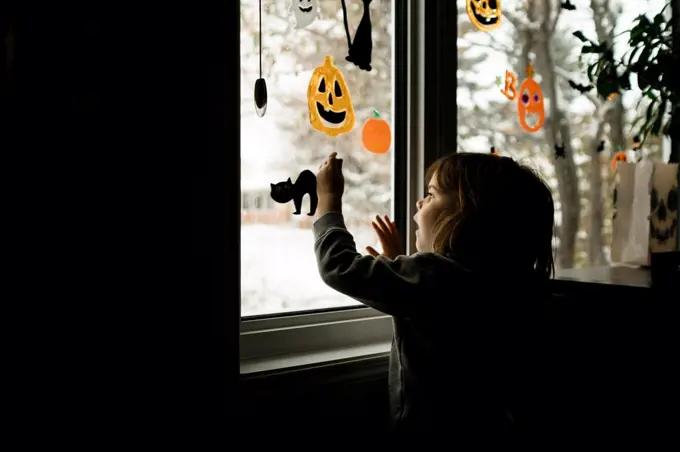 Young girl putting Halloween decorations up on windows in living room