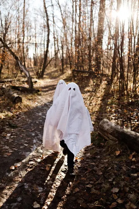 Two children in ghost costumes running in a park in the fall